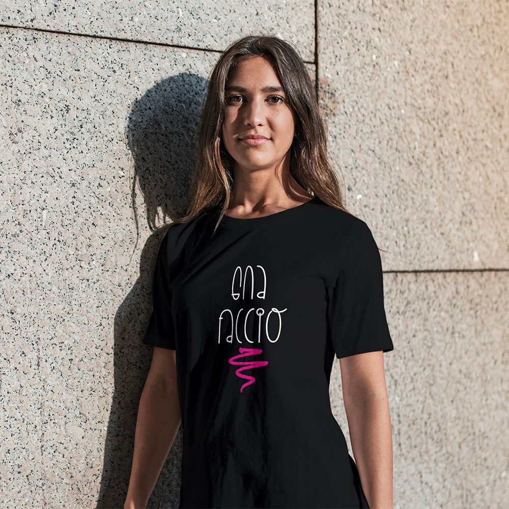 La T-shirt nera Gna faccio di Il mio negozio è appesa a una parete di legno, con la scritta "GNA FACCIO" in bianco con un ghirigoro rosa e un piccolo logo nero sul petto a sinistra, ideale per idee regalo o magliette personalizzate divertenti.