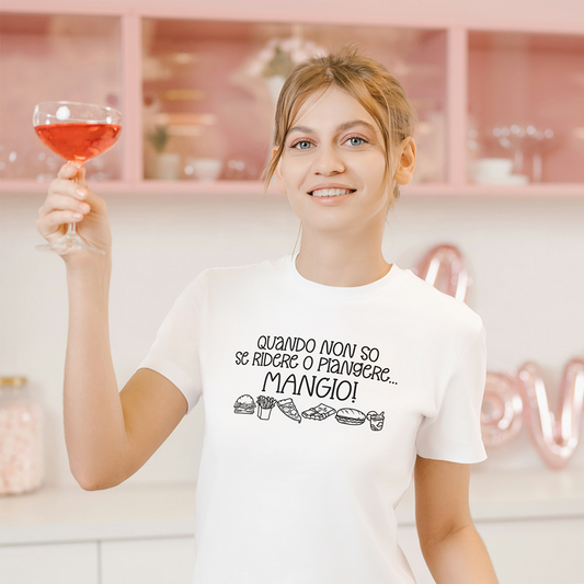 La T-shirt Mangio de Il mio negozio è caratterizzata dal testo in italiano "Quando non so se ridere o piangere... MANGIO!" e simpatica food art. Maglietta nera divertente, ideale come regalo per chi ama le magliette personalizzate. Mostrato su superficie in legno chiaro.