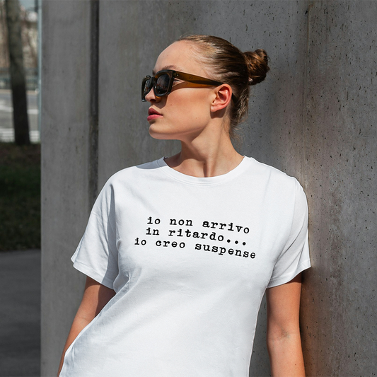 Una donna con occhiali da sole e una T-shirt Ritardo con testo italiano de Il mio negozio si appoggia a un muro di cemento, mettendo in evidenza magliette personalizzabili, ideali per aggiungere stile o come regalo originale.