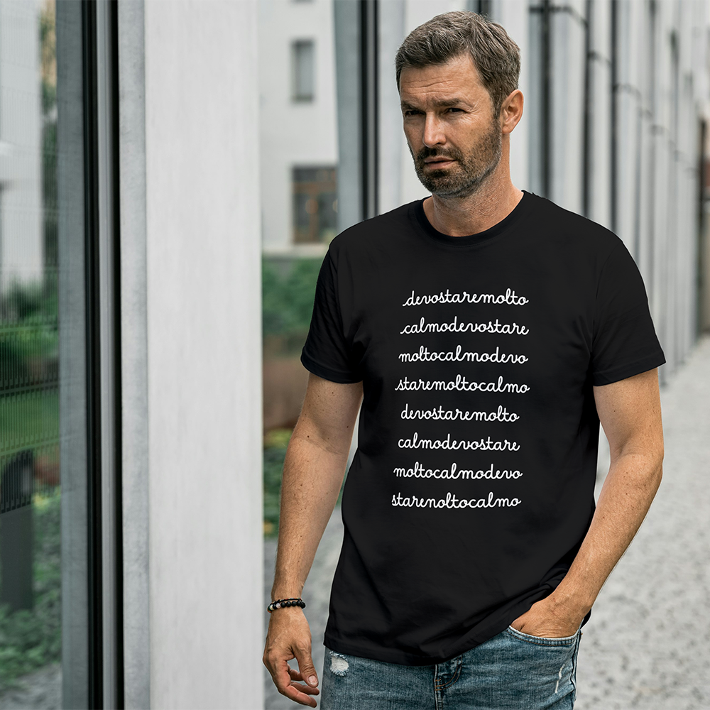 Due magliette Calma o Calmo de Il mio negozio, una bianca e una nera, sono appese a grucce di legno con viti frondose sopra. Queste divertenti magliette italiane sono idee regalo uniche per chi ama lo stile originale.