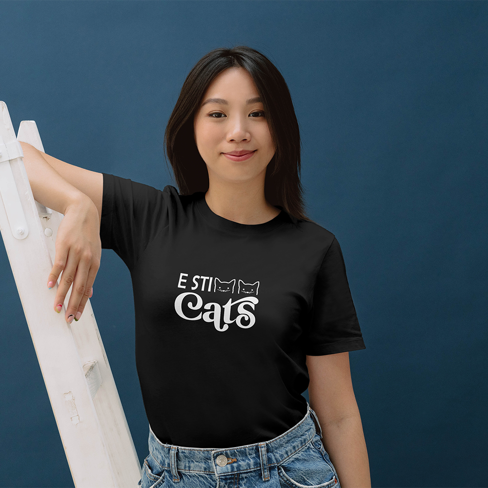 La T-shirt E sticats de Il mio negozio è caratterizzata dal testo nero "E STI Cats" con facce di gatto nel design, perfetto per i fan delle magliette personalizzate divertenti! Da abbinare a sneakers rosa e a un cerchietto nero scintillante con orecchie da Minnie Mouse.