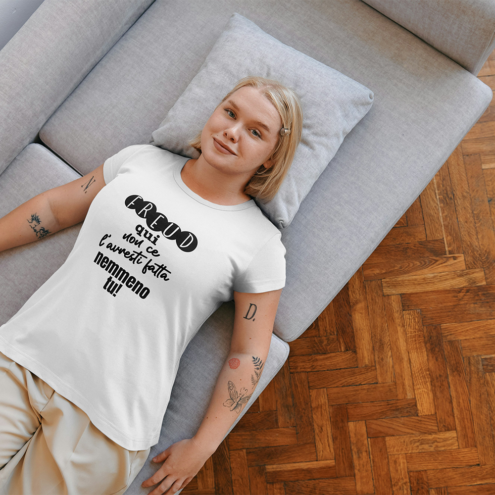 La T-shirt Freud de Il mio negozio è una maglietta bianca ripiegata con il testo italiano "Freud qui non ce l'hai fatta nemmeno tu!" visualizzato su una superficie nera; sullo sfondo compare una tazza rosa con puntini neri, che la rende una perfetta idea regalo.