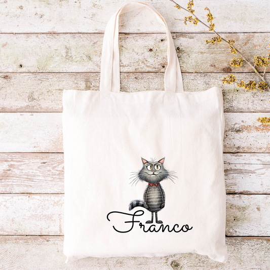 Borsa tote beige con un gatto grigio a fumetti e la scritta "Franco" in corsivo su uno sfondo di legno rustico, ideale da abbinare allo Specchietto Tondo di In Casa di Ale o ad altri accessori personalizzati.