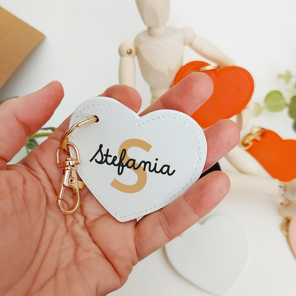 Una mano regge un In Casa di Ale Portachiavi Cuore in pelle PU con la scritta "Stefania", accanto a portachiavi arancioni e bianchi.