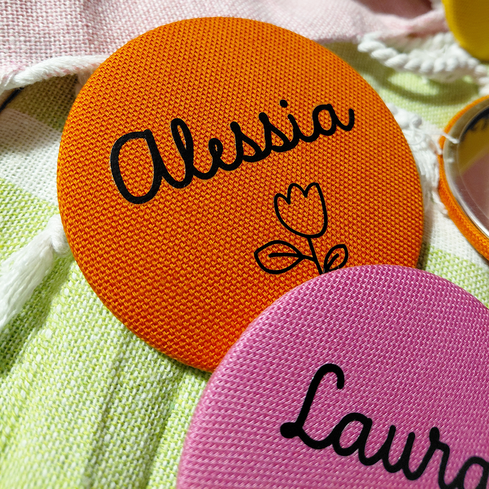Distintivo in tessuto arancione con Alessia e tulipani accanto a un distintivo Laura rosa: ideale se abbinato allo "Specchietto tondo colorato e personalizzato" di In Casa di Ale per un divertente tocco di colore personalizzato.