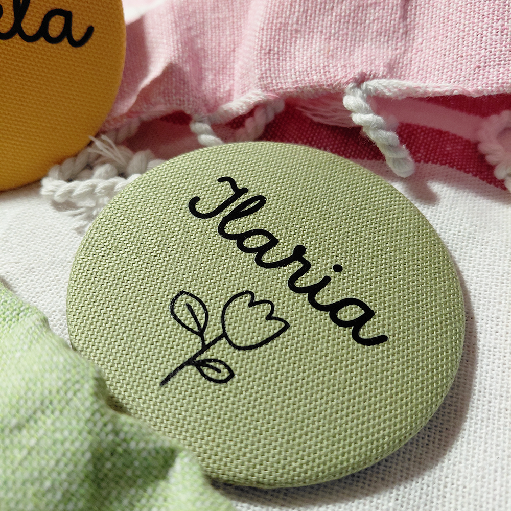 Un badge rotondo in tessuto con Ilaria e un'illustrazione floreale sul verde, perfetto da abbinare al vostro Specchietto tondo colorato e personalizzato di In Casa di Ale.