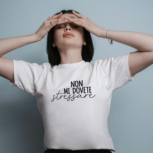 Una donna che indossa la T-shirt Stressare di Il mio negozio, con testo in italiano, si tocca la fronte e sembra stressata su uno sfondo a tinta unita.