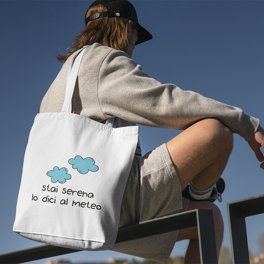 Tote bag con illustrazione di nuvole e scritta Stai serena lo dici al meteo, shopper in cotone bianca indossata all’aperto
