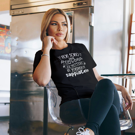Una donna seduta in una cucina moderna indossa la T-shirt Vivavoce de Il mio negozio, una maglietta nera personalizzata con testo italiano sul davanti.