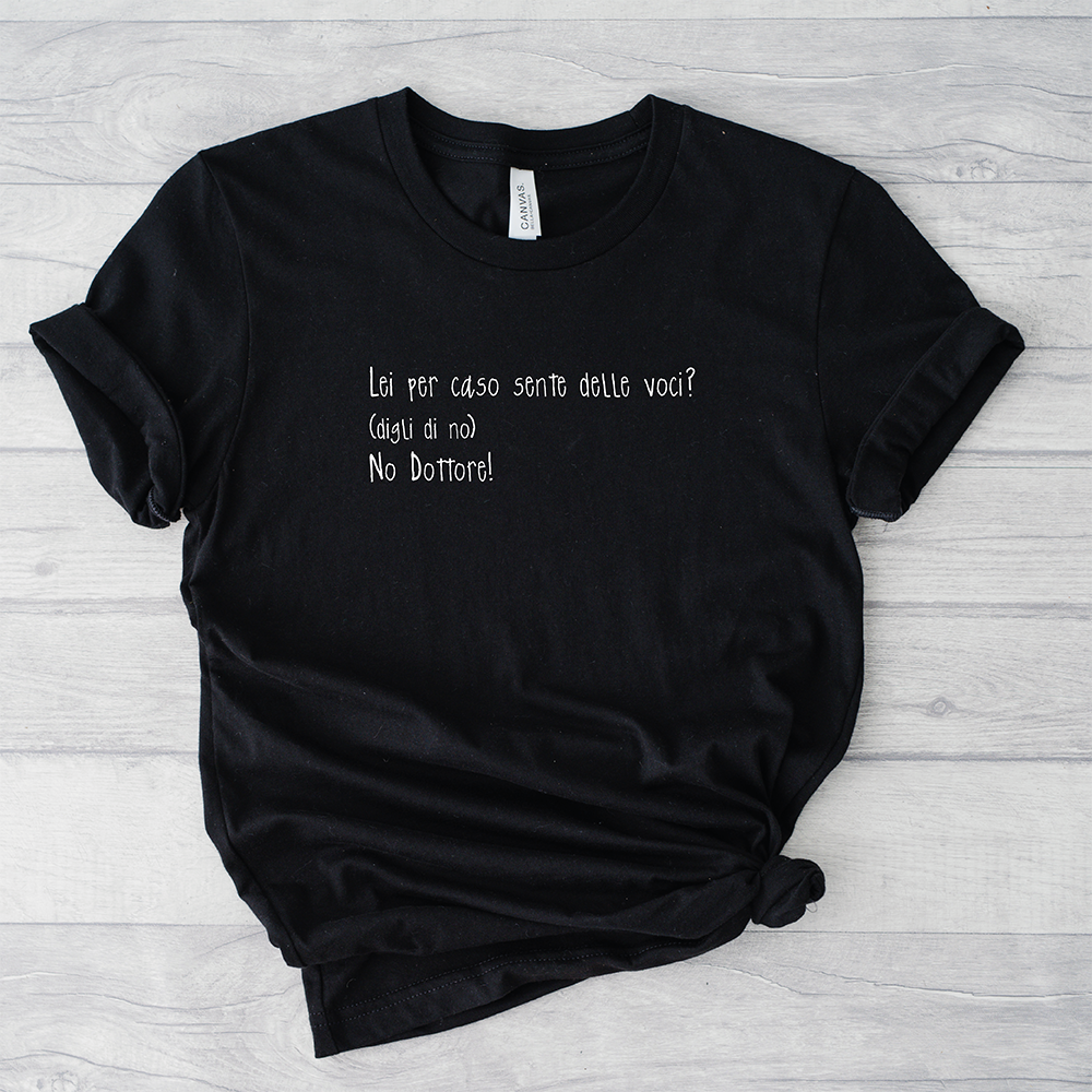 Il mio negozio T-shirt Sento voci nere con la scritta italiana "Lei per caso sente delle voci? (dica di no) No Dottore!" su sfondo in legno chiaro.