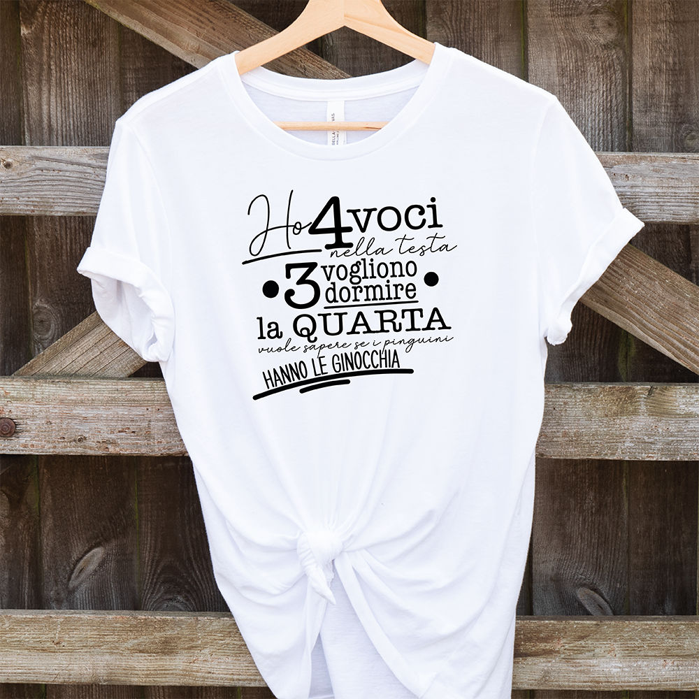 La T-shirt 4 voci de Il mio negozio è appesa a una staccionata di legno. Questa maglietta bianca personalizzata riporta in nero il testo italiano: Ho 4 voci nella testa. 3 vogliono dormire, la quarta vuole sapere se i pinguini hanno le ginocchia.