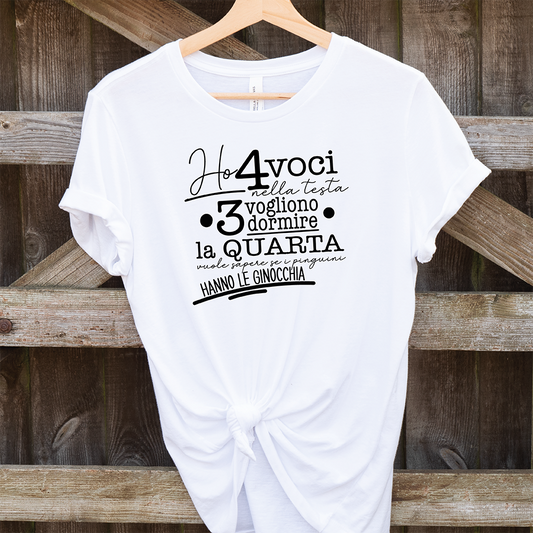 La T-shirt 4 voci de Il mio negozio è appesa a una staccionata di legno. Questa maglietta bianca personalizzata riporta in nero il testo italiano: Ho 4 voci nella testa. 3 vogliono dormire, la quarta vuole sapere se i pinguini hanno le ginocchia.