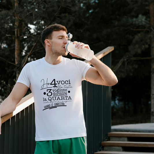 La T-shirt 4 voci de Il mio negozio è appesa a una staccionata di legno. Questa maglietta bianca personalizzata riporta in nero il testo italiano: Ho 4 voci nella testa. 3 vogliono dormire, la quarta vuole sapere se i pinguini hanno le ginocchia.