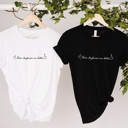 Due T-shirt Dubito Donna de Il mio negozio, una bianca e una nera con la scritta "Përur slogjanme me dashte" in corsivo, appese a grucce di legno su sfondo bianco, ideali per gli appassionati di magliette personalizzate divertenti.