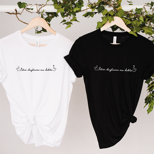Due T-shirt Dubito Donna de Il mio negozio, una bianca e una nera con la scritta "Përur slogjanme me dashte" in corsivo, appese a grucce di legno su sfondo bianco, ideali per gli appassionati di magliette personalizzate divertenti.