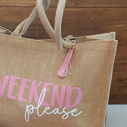 Dettaglio della borsa in juta con scritta Weekend Please e nappina decorativa rosa e bianca.