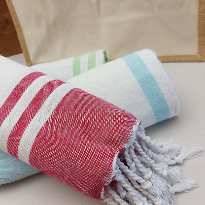 Dettaglio di teli mare fouta arrotolati in diversi colori, con righe bianche e frange decorative.