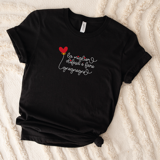 Una "T-shirt Gnegnegne" nera di In Casa di Ale, con scritte bianche e un palloncino rosso a forma di cuore, una delle nostre magliette personalizzate divertenti, posata su una superficie color crema.