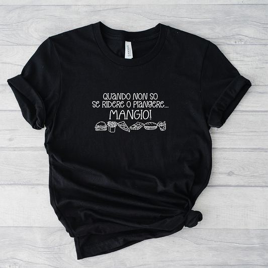 La T-shirt Mangio de Il mio negozio è caratterizzata dal testo in italiano "Quando non so se ridere o piangere... MANGIO!" e simpatica food art. Maglietta nera divertente, ideale come regalo per chi ama le magliette personalizzate. Mostrato su superficie in legno chiaro.