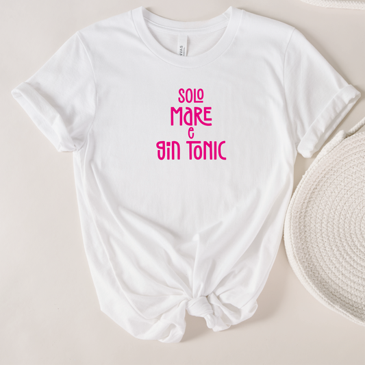 La T-shirt Mare e GinTonic de Il mio negozio, bianca con scritta rosa "SOLO MARE & GIN TONIC", è caratterizzata da maniche arrotolate e orlo annodato, perfetta per chi ama le magliette personalizzate divertenti. Accanto a un cappello intrecciato su sfondo chiaro.