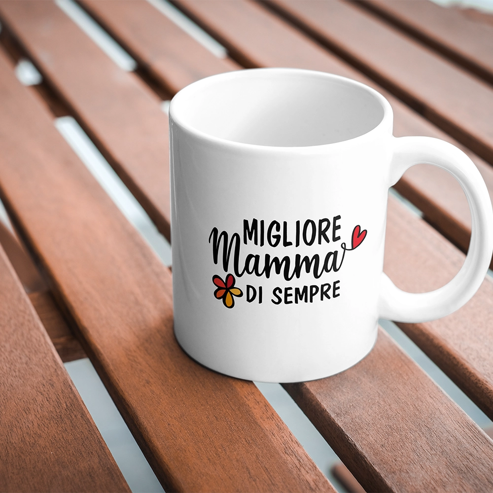 Tazza bianca dedicata alla mamma con scritta Migliore Mamma di sempre, fotografata su tavolo in legno.