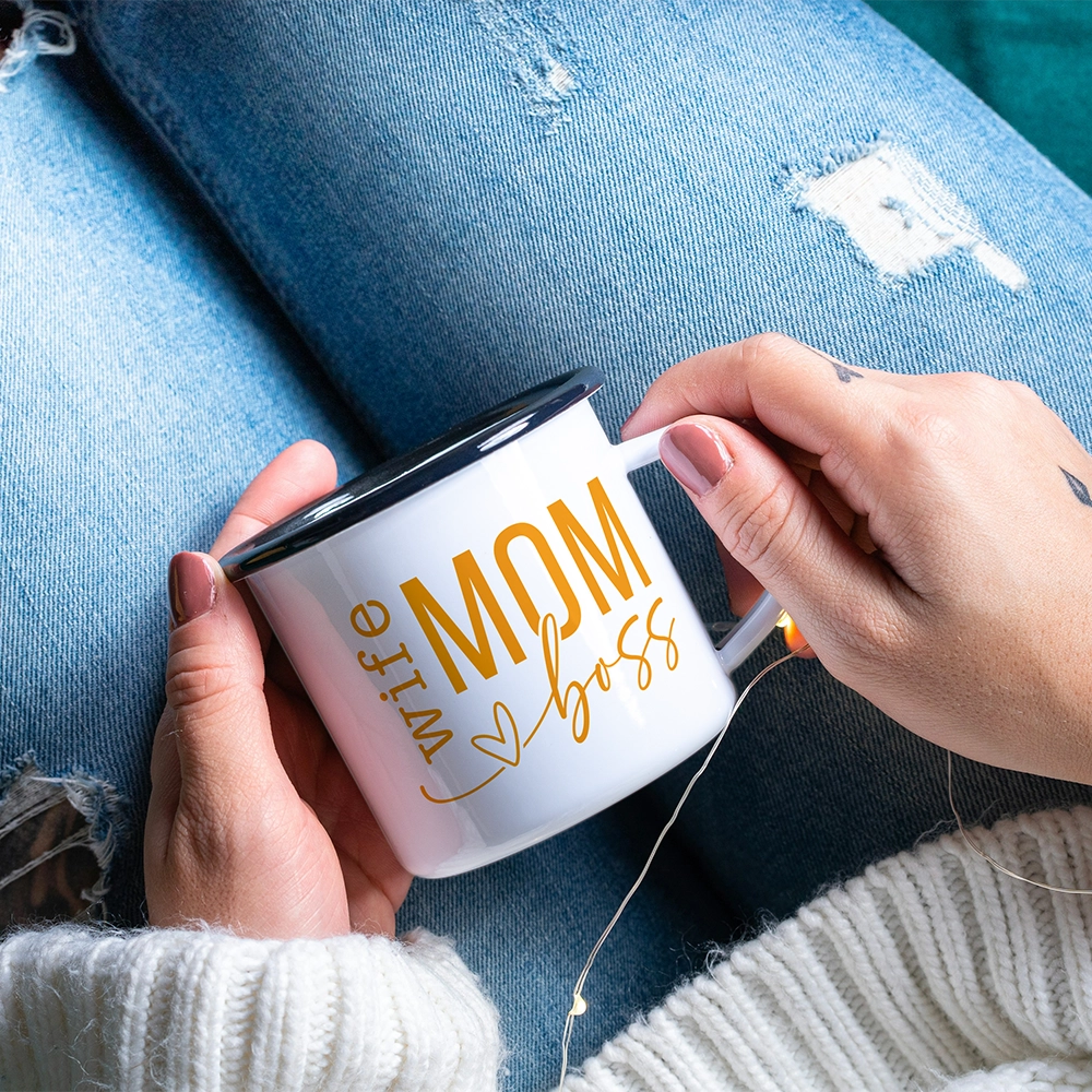 Mug in alluminio dedicata alla mamma con scritta Wife Mom Boss in giallo, tenuta tra le mani con lucine decorative.