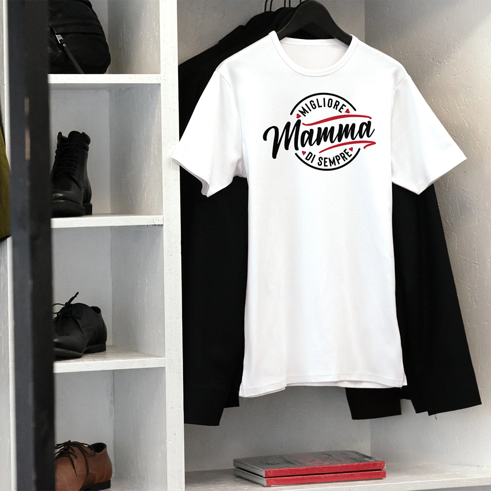 T-shirt bianca per la mamma con scritta Migliore Mamma di sempre, appesa in ambientazione minimal.