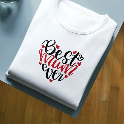T-shirt bianca per la mamma con scritta Best Mum Ever e piccoli cuori rossi, piegata su piano scuro.