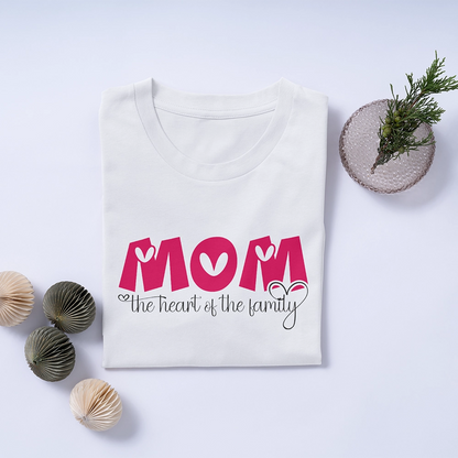 T-shirt bianca dedicata alla mamma con scritta Mom The Heart of the Family, fotografata piegata con decorazioni delicate.