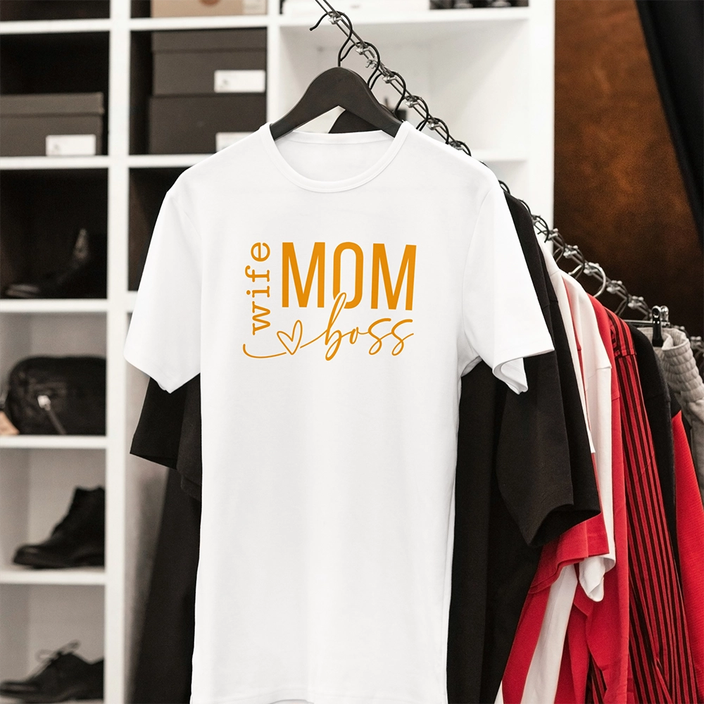 T-shirt bianca dedicata alla mamma con scritta Wife Mom Boss, appesa su gruccia in ambientazione guardaroba.