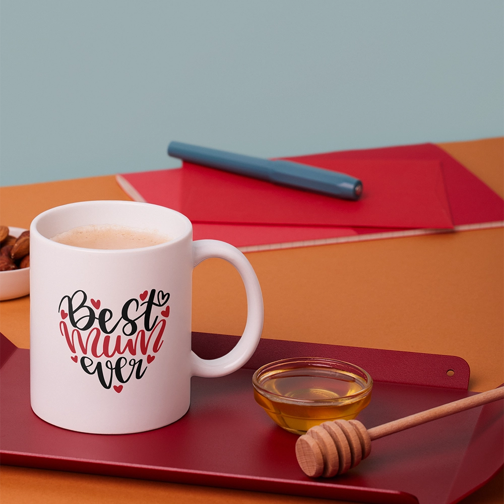 Tazza bianca per la mamma con scritta Best Mum Ever, ambientata su vassoio con miele e bevanda calda.
