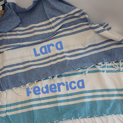 Teli mare fouta personalizzati nei colori blu e acquamarina, con nomi stampati e frange laterali.