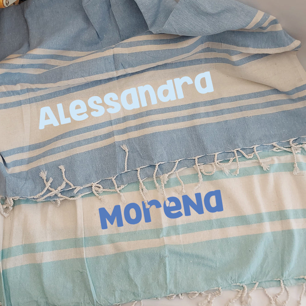 Due teli mare fouta personalizzati nei colori celeste e azzurro, con esempio di nome stampato.