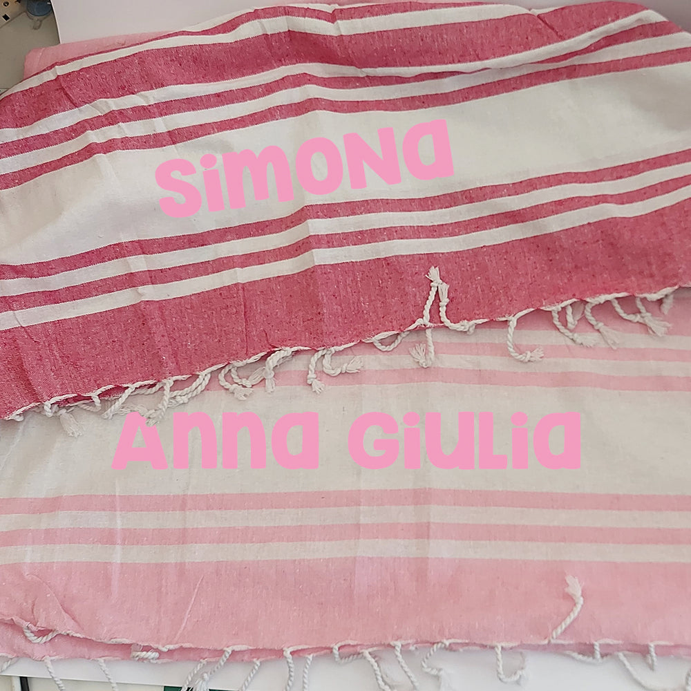 Due teli mare fouta personalizzati nei colori rosa e fucsia, con esempi di nomi stampati al centro.
