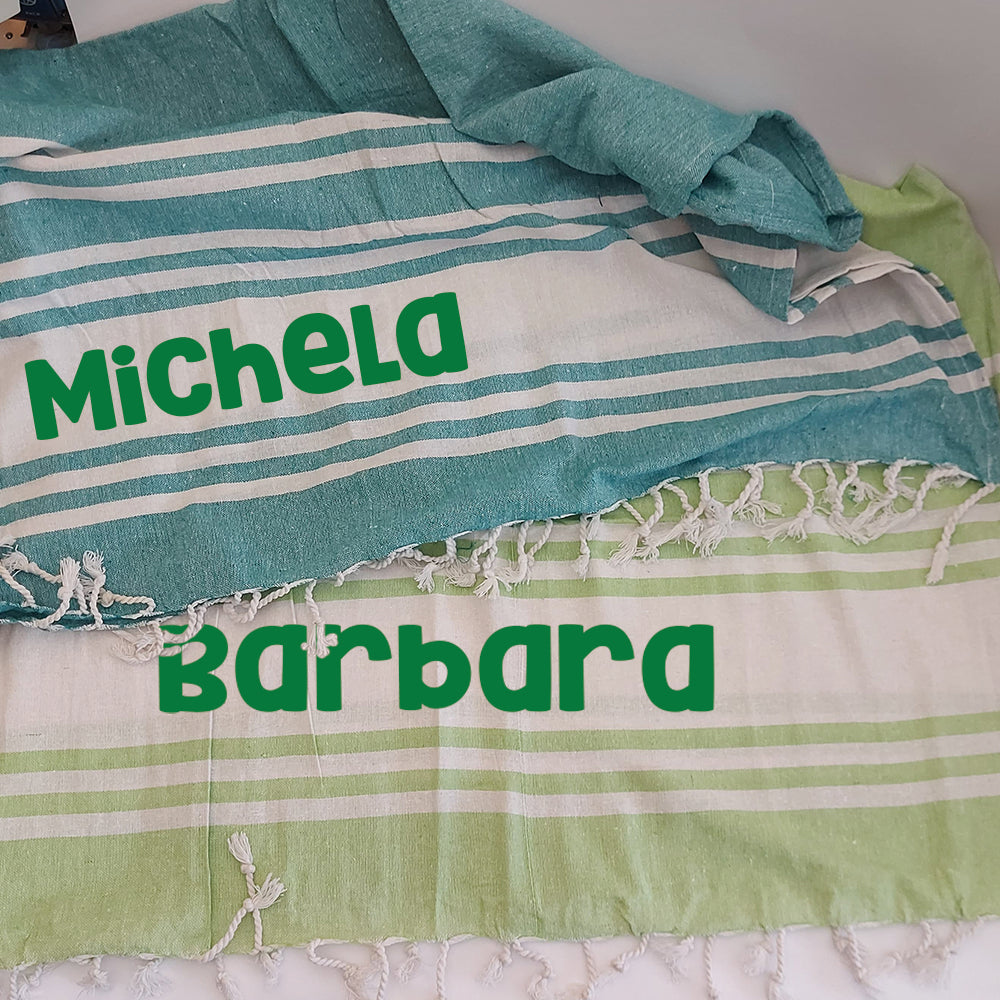 Teli mare fouta personalizzati nei colori verde e verde chiaro, con nomi stampati e dettagli a righe bianche.