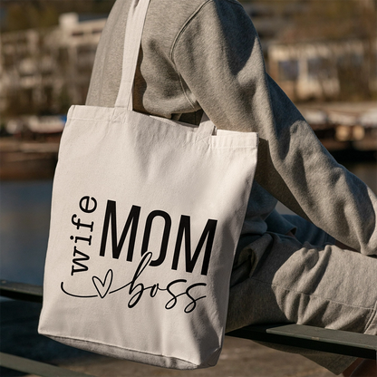 Tote bag bianca dedicata alla mamma con scritta Wife Mom Boss nera, portata a spalla in ambientazione outdoor.
