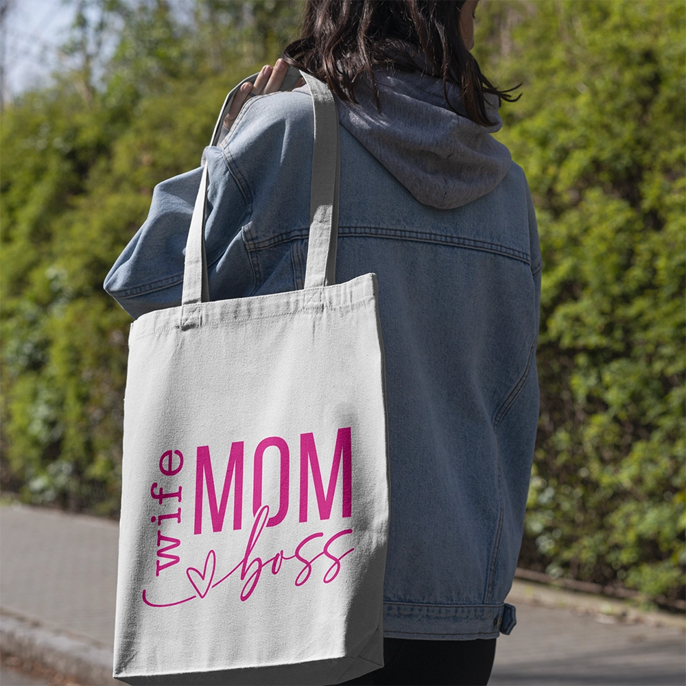Tote bag bianca dedicata alla mamma con scritta Wife Mom Boss in rosa, portata a spalla in esterno.