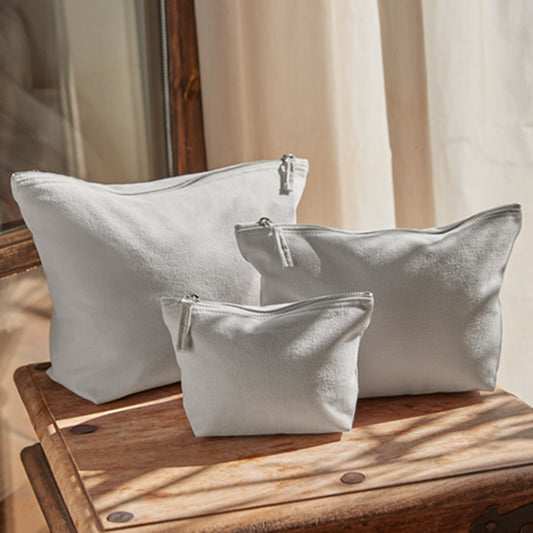 Set di tre pochette in cotone canvas naturale nelle tre misure disponibili, fotografate insieme su tavolino in legno.