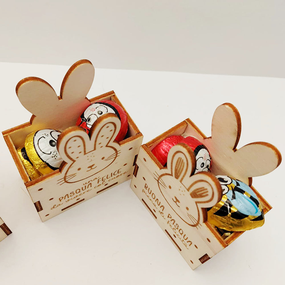 Vista dall’alto di scatoline di Pasqua in legno con coniglietto inciso e 4 cioccolatini assortiti