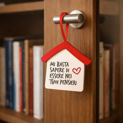 Casetta in legno appesa a una maniglia con nastro rosso, frase “Mi basta sapere di essere nei tuoi pensieri”
