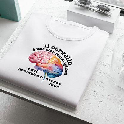 La T-shirt bianca Cervello de Il mio negozio, con un cervello colorato e la frase "Il cervello è una cosa meravigliosa, tutti dovrebbero averne uno!", è appoggiata vicino agli occhiali da sole su una superficie strutturata: una divertente maglietta personalizzata!.