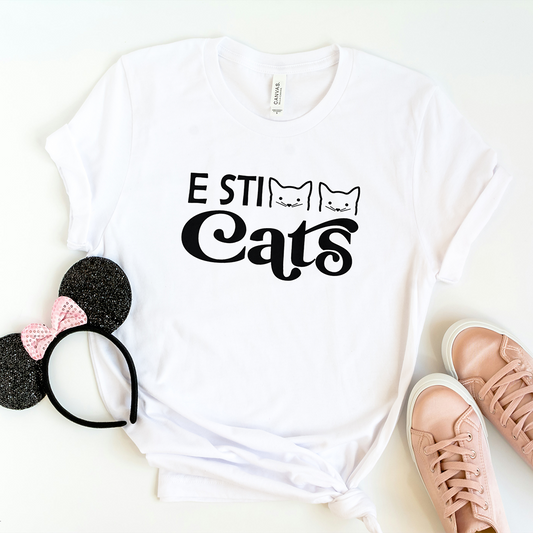 La T-shirt E sticats de Il mio negozio è caratterizzata dal testo nero "E STI Cats" con facce di gatto nel design, perfetto per i fan delle magliette personalizzate divertenti! Da abbinare a sneakers rosa e a un cerchietto nero scintillante con orecchie da Minnie Mouse.