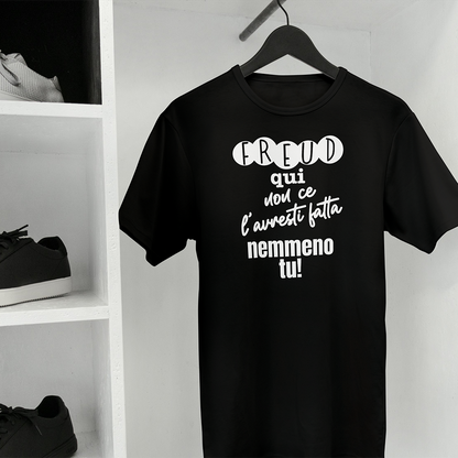 La T-shirt Freud de Il mio negozio è una maglietta bianca ripiegata con il testo italiano "Freud qui non ce l'hai fatta nemmeno tu!" visualizzato su una superficie nera; sullo sfondo compare una tazza rosa con puntini neri, che la rende una perfetta idea regalo.