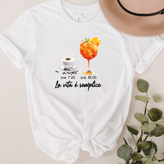 La T-shirt La vita è semplice di Il mio negozio ha illustrazioni di una tazza di caffè (ore 7.00) e un cocktail arancione (ore 18.00), con la frase "La vita è semplice". Ideale per chi ama magliette divertenti e personalizzate.