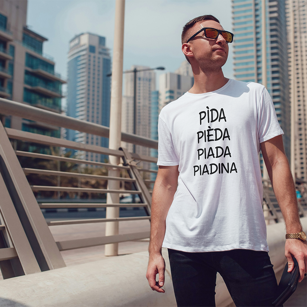 Un uomo con gli occhiali da sole e la T-shirt bianca Piadina de Il mio negozio, con il testo PIDA, PIEDA, PIADA, PIADINA, è in piedi su un ponte della città - un ideale regalo originale.