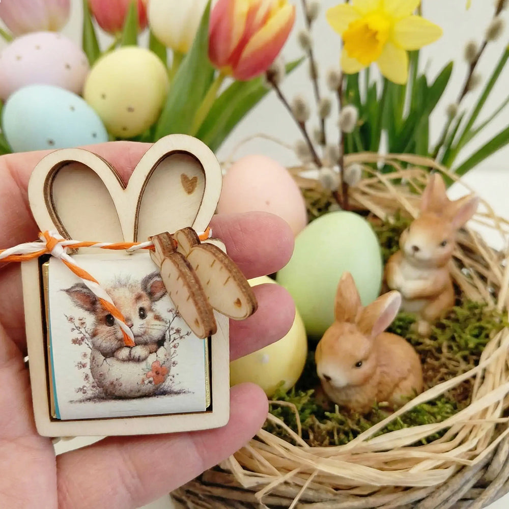 Porta cioccolatino pasquale in legno mostrato in mano vicino a nido decorativo con coniglietti e uova colorate