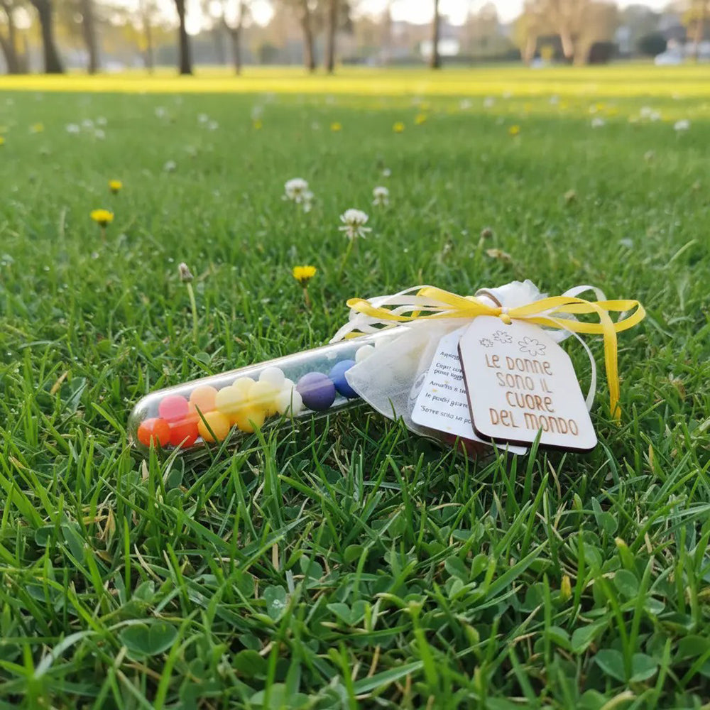 Provetta regalo Festa della Donna fotografata sul prato, con tag in legno inciso e nastri gialli