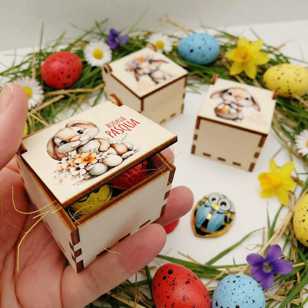 Scatolina pasquale in legno tenuta in mano con cioccolatini interni e decorazioni di Pasqua sullo sfondo
