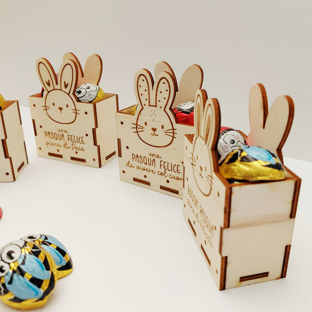 Vista laterale obliqua di scatoline di Pasqua in legno con coniglietto inciso e cioccolatini assortiti