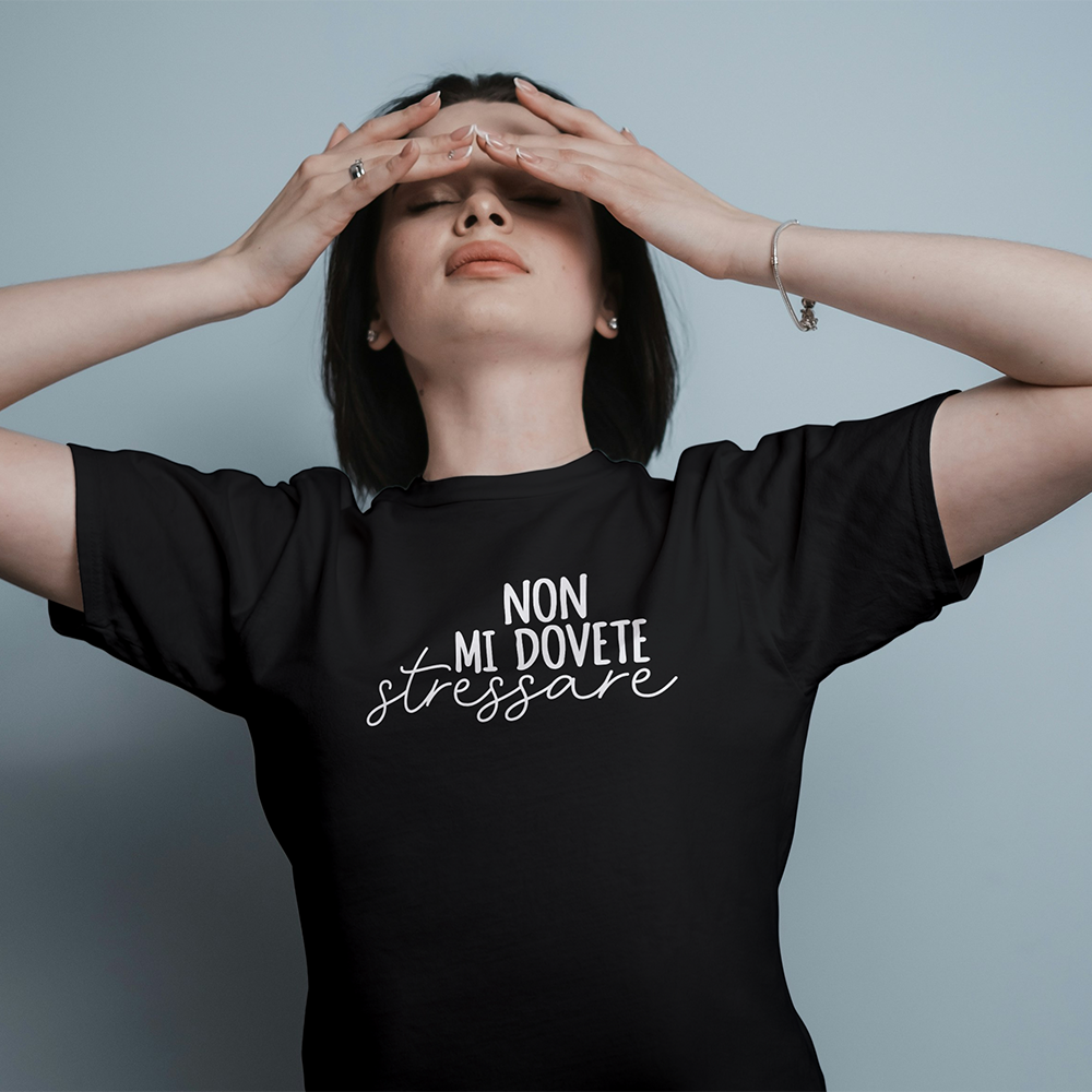 Una donna indossa la "T-shirt Stressare" nera de Il mio negozio, con testo in italiano, con le mani sulla fronte e l'aria stressata.
